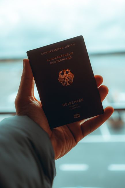 Mano sosteniendo un pasaporte frente al ventanal de un aeropuerto